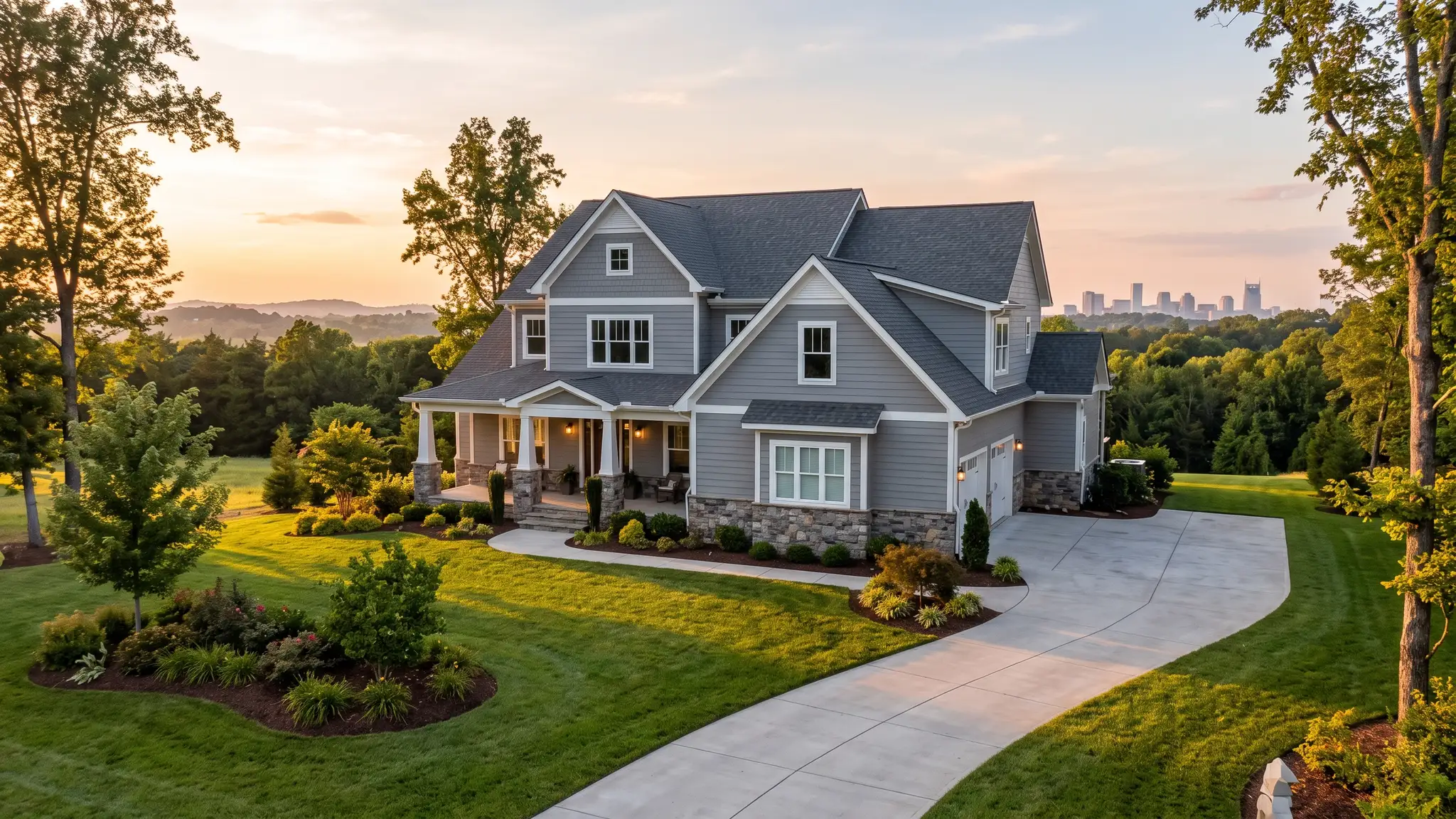 Music City Siding | Siding installation and repair in Nashville, TN A handsome Tennessee home with fresh gray lap siding, white trim and a stone base at golden hour with the Nashville skyline softly visible in the distance